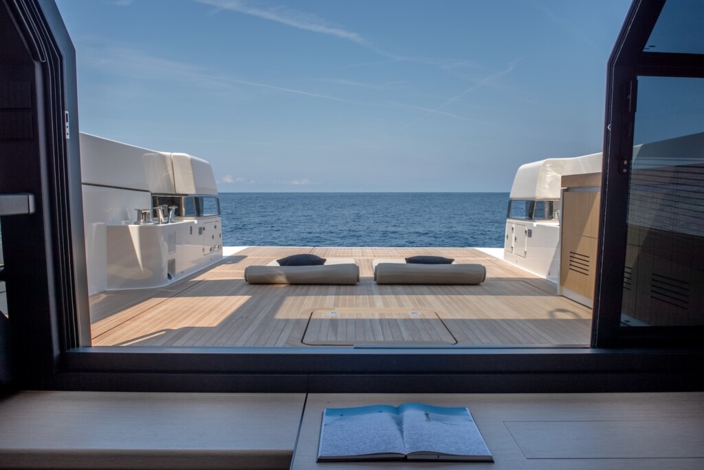 View thought the open doors onto the light wooden deck of a motor yacht looking towards the horizon across calm water