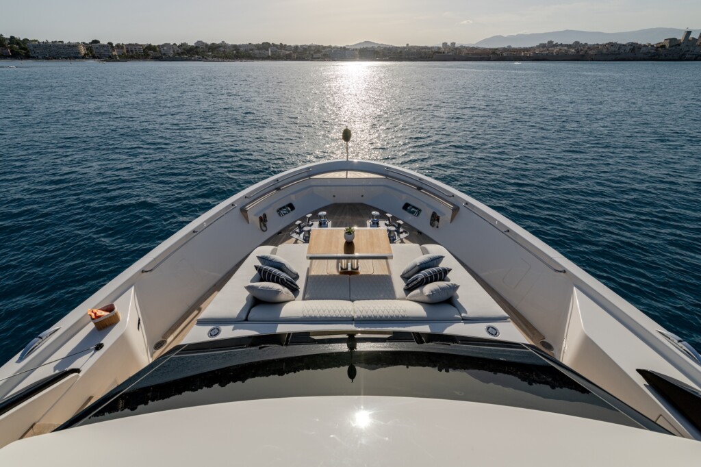 Bow of a white hulled motor yacht with seating, cushions and a small wooden table